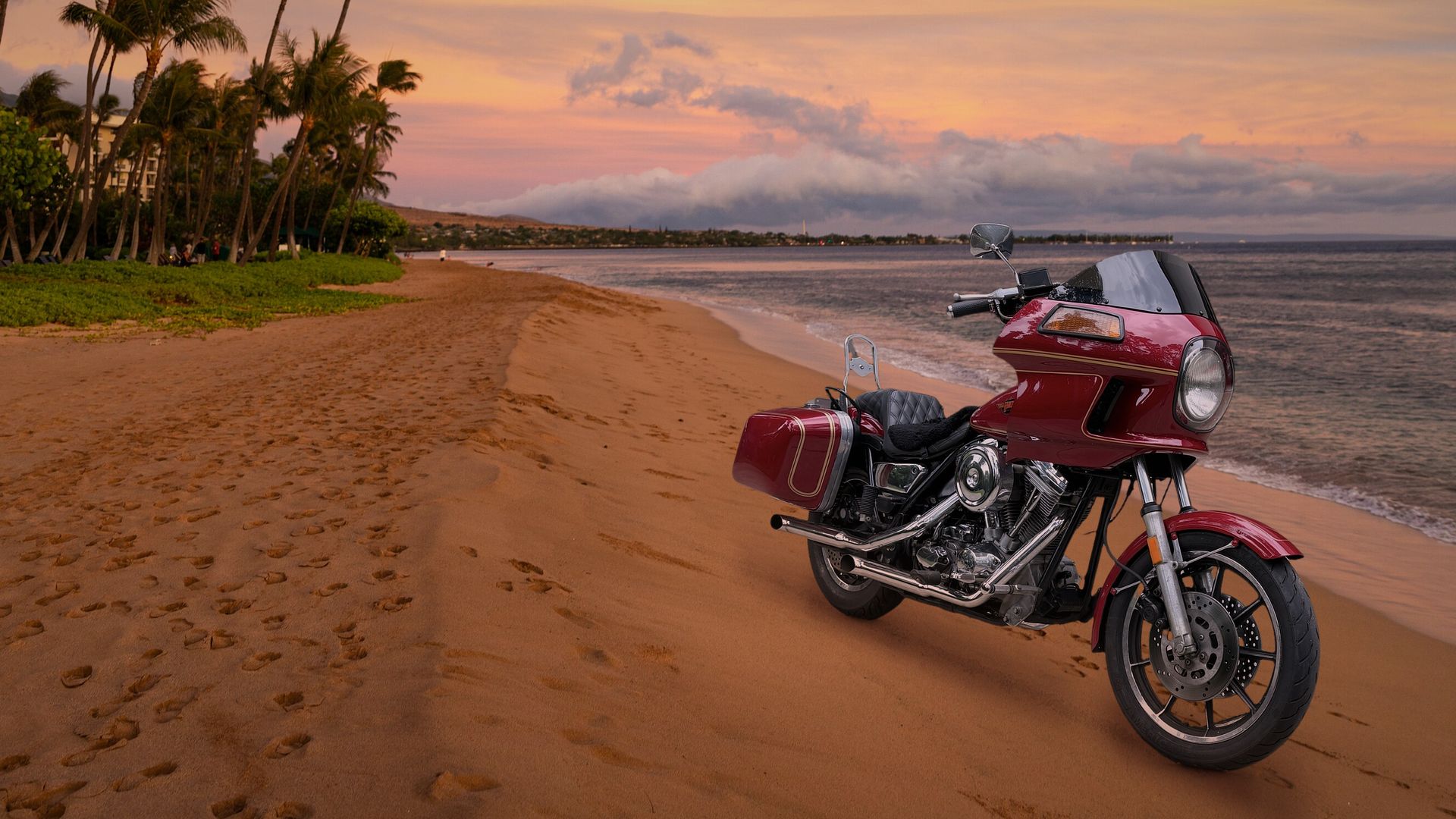 A red 1985 Harley-Davidson FXRT with its fairing and saddlebags, parked on a beach at dusk under a pink sky.