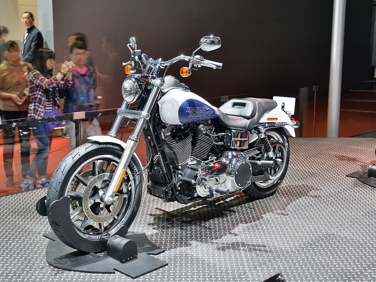 A white and blue Harley-Davidson Dyna Low Rider on a display stand at a motor show