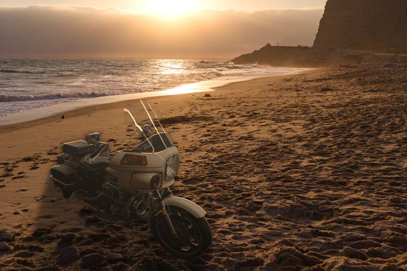 A white 1984 FXRP police bike on a beach at sunset, a composite image. Not the bike for sale.
