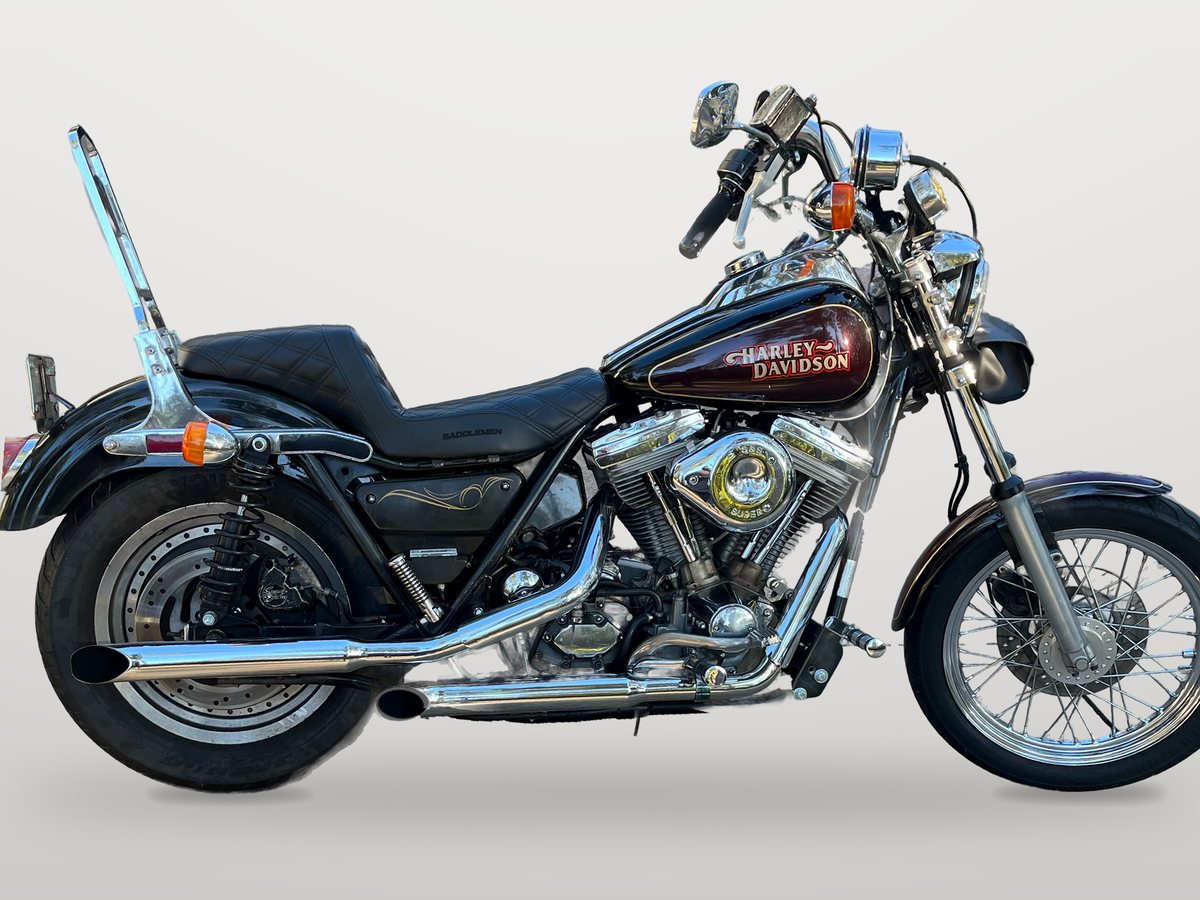 Side view of a black and burgundy Harley-Davidson FXR with a chrome sissy bar and a laced front wheel, on a plain gray background