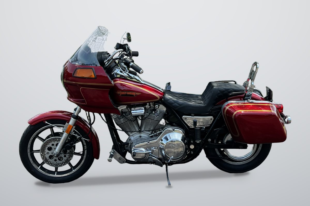 A red Harley-Davidson FXRT with its fairing and hard saddlebags, seen from the left side on a plain grey backdrop