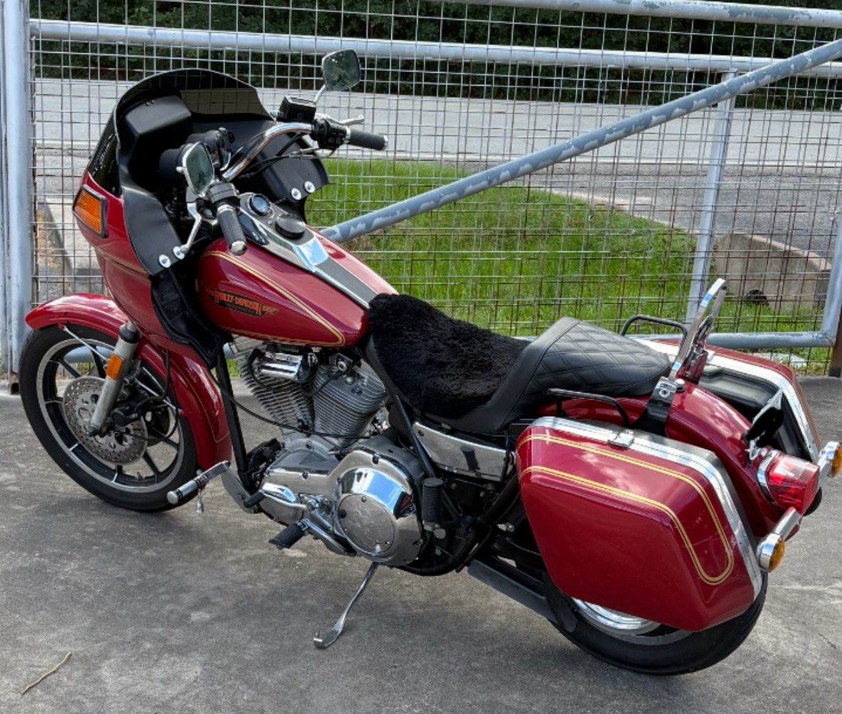 A red 1985 Harley-Davidson FXRT with gold pinstripes, fairing and hard saddlebags parked on concrete by a fence